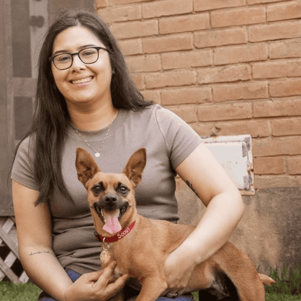 A young woman sitting with a small brown dog in her lap