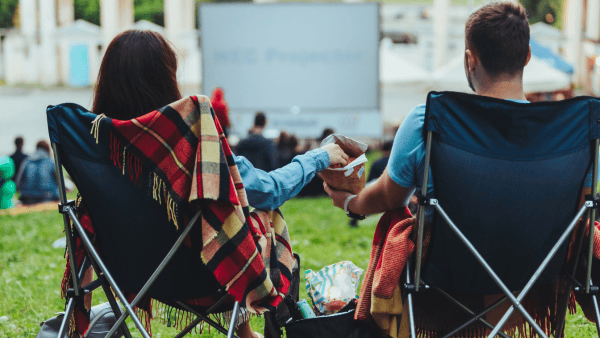 A man and woman sitting in lawn chairs outside in front of a movie screen