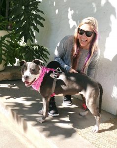 Macie smiles as she kneels next to a medium sized dog.  Both look towards the camera.