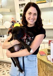 A young woman in a Love-A-Bull shirt holds up a black pit bull puppy and stares at the camera.