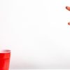 A person throwing a ping pong ball into red solo cups