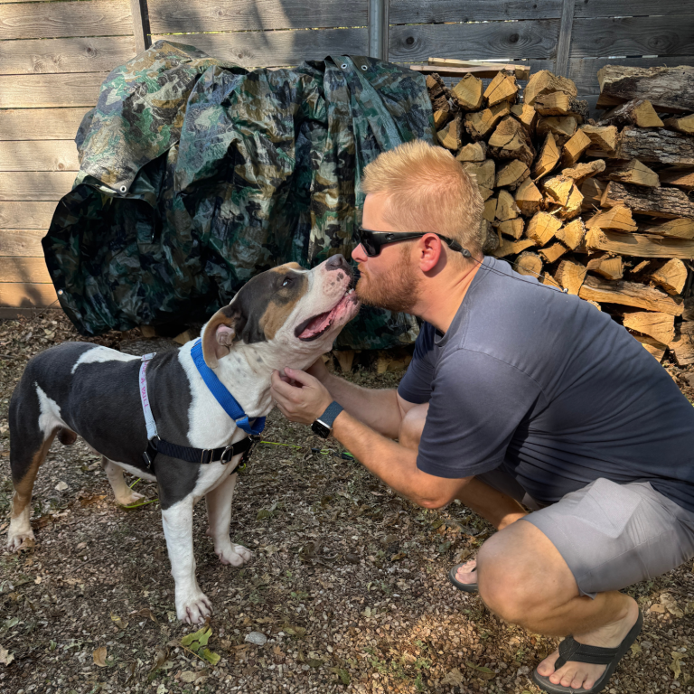 A man giving a pitbull dog a kiss