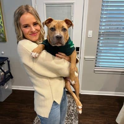 Woman standing inside a house while holding a dog.