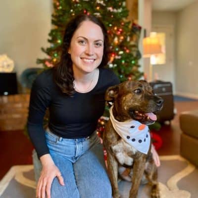 Woman sitting next to a dog in front of a Christmas tree.