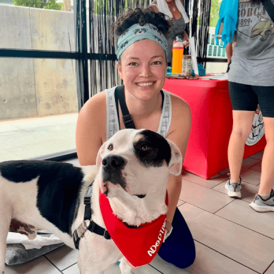 Young woman sitting behind a black and white dog that is wearing a red bandana