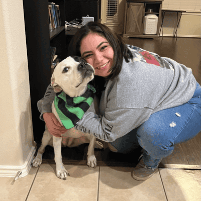 A young woman hugging a black and white pit bull dog wearing a green and black striped bandana