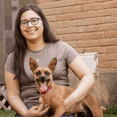 A young woman sitting with a small brown dog in her lap