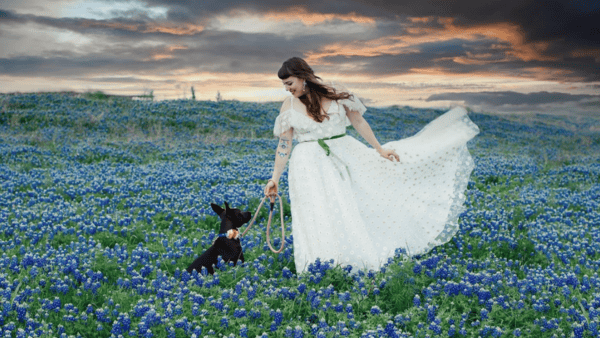 Woman standing in a field of bluebonnets with her dog.