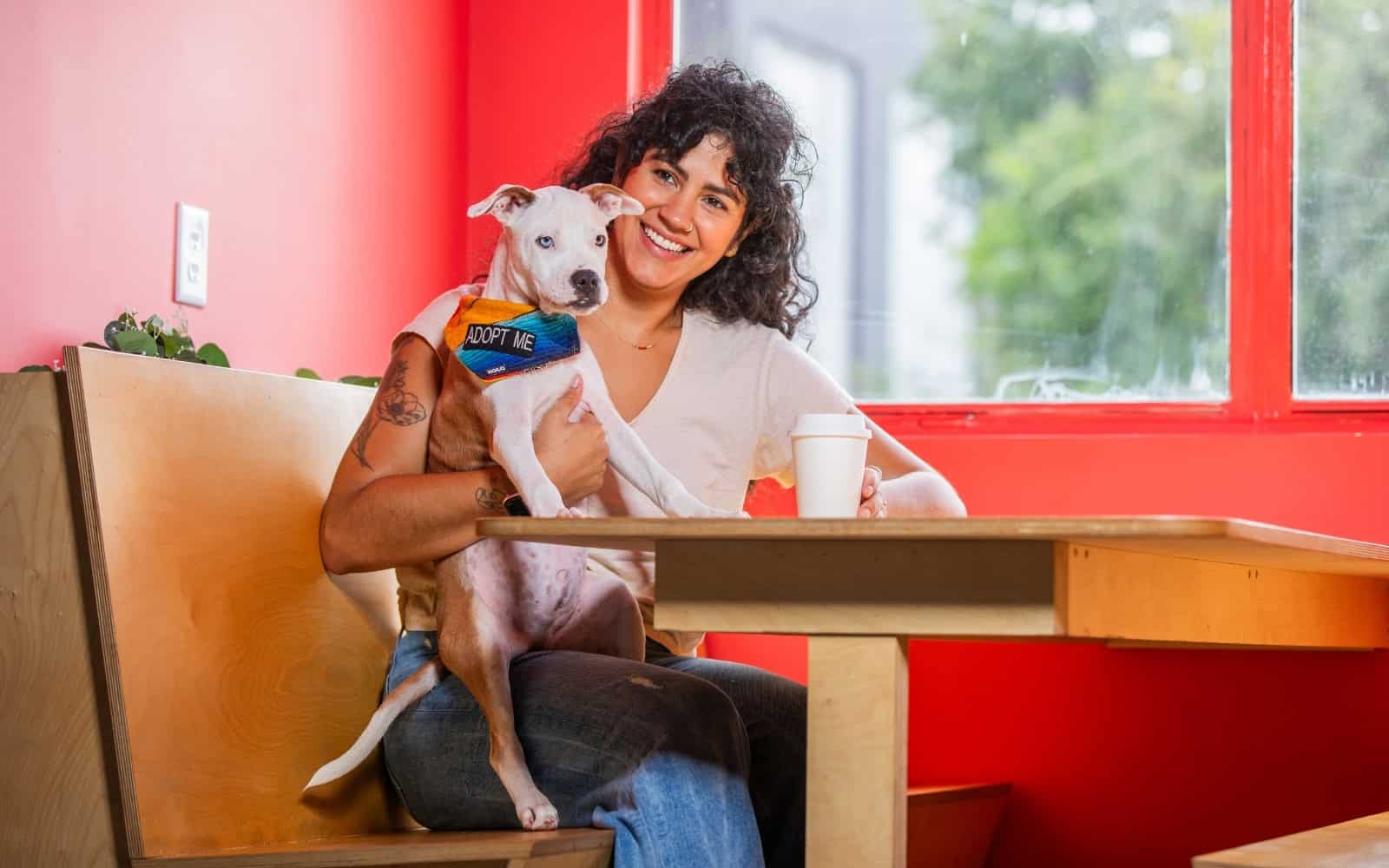 A woman holding a white pit bull puppy while sitting at a cafe table.